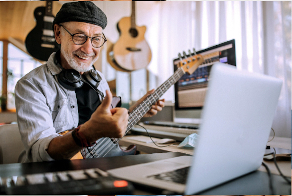 Smilende mann spiller bassgitar under en nettbasert musikktime og gir tommel opp til kameraet.
